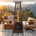 A bronze Capri heater standing outdoors in front of sofas.